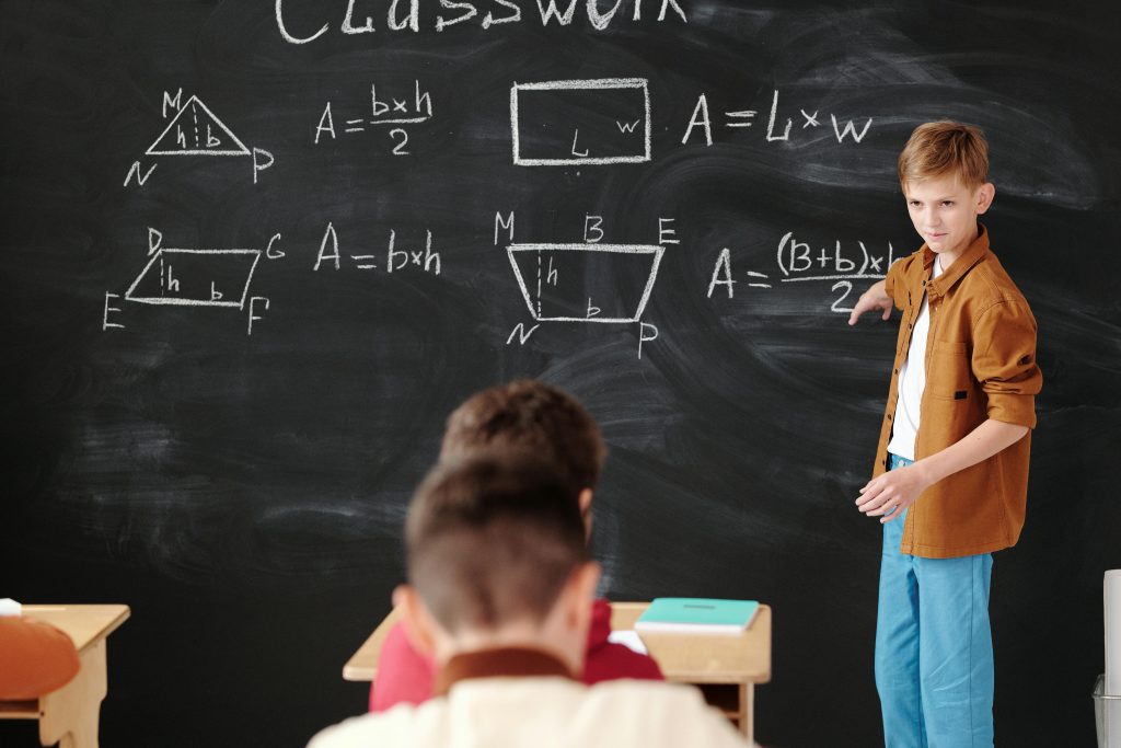 A young student explains math formulas on a blackboard during classwork.